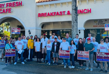 Group of supporters outside a cafe, posing with Maple s campaign signs in front of a Breakfast & Lunch storefront.