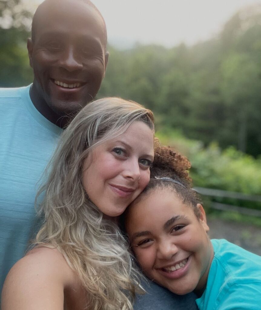 Smiling family selfie outdoors: a man, woman, and girl close together in a park setting